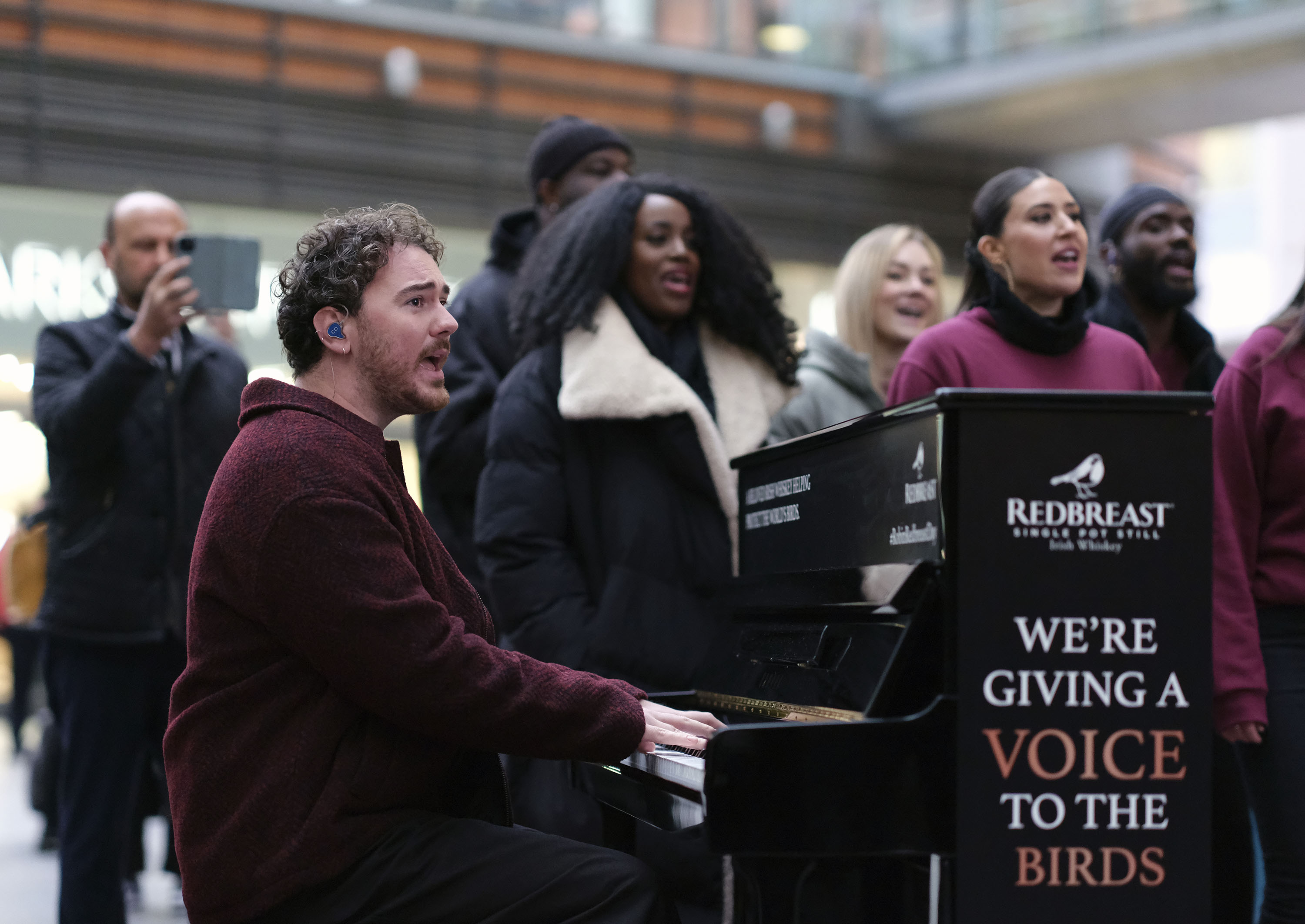 Irish singer-songwriter Cian Ducrot and a choir surprise London commuters with a performance to raise awareness for the loss of morning bird song and the decline in many bird populations at Victoria Station on Thursday, Nov. 16, 2023, in London. (Michael Knief/AP Images for Redbreast Irish Whiskey)