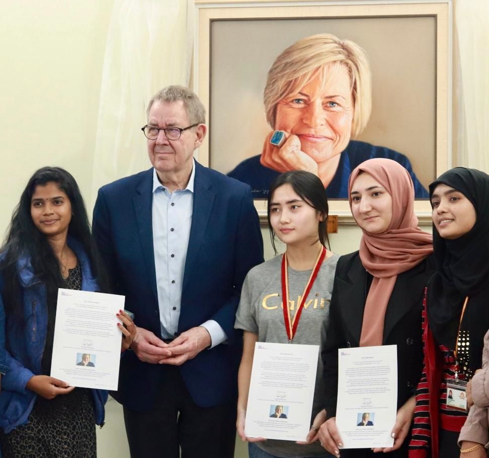 Prime Minister Poul Nyrup Rasmussen with Lone Dybkjaer Scholars in front of a portrait of the late Lone Dybkjaer at AUW’s Mahsa Amini Center